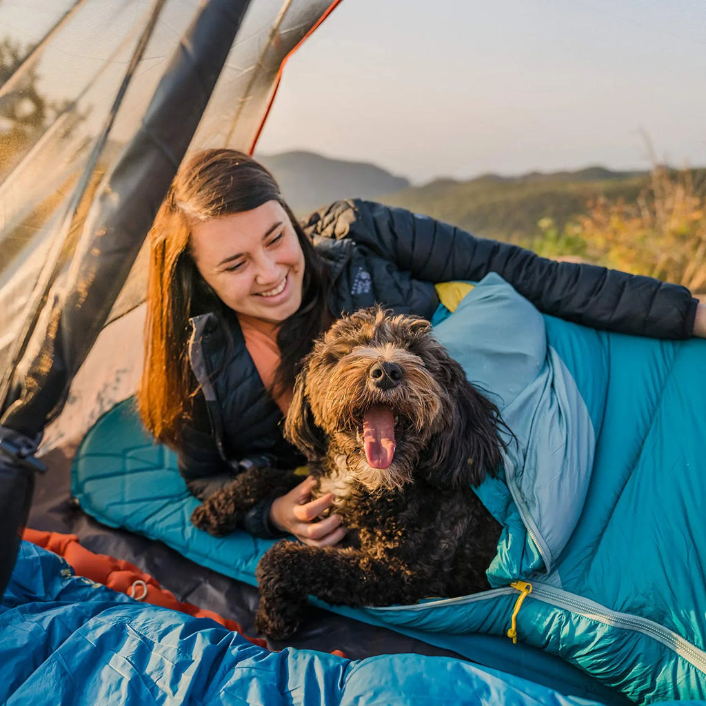 Personne et chien installés dans un sac de couchage en plein air.